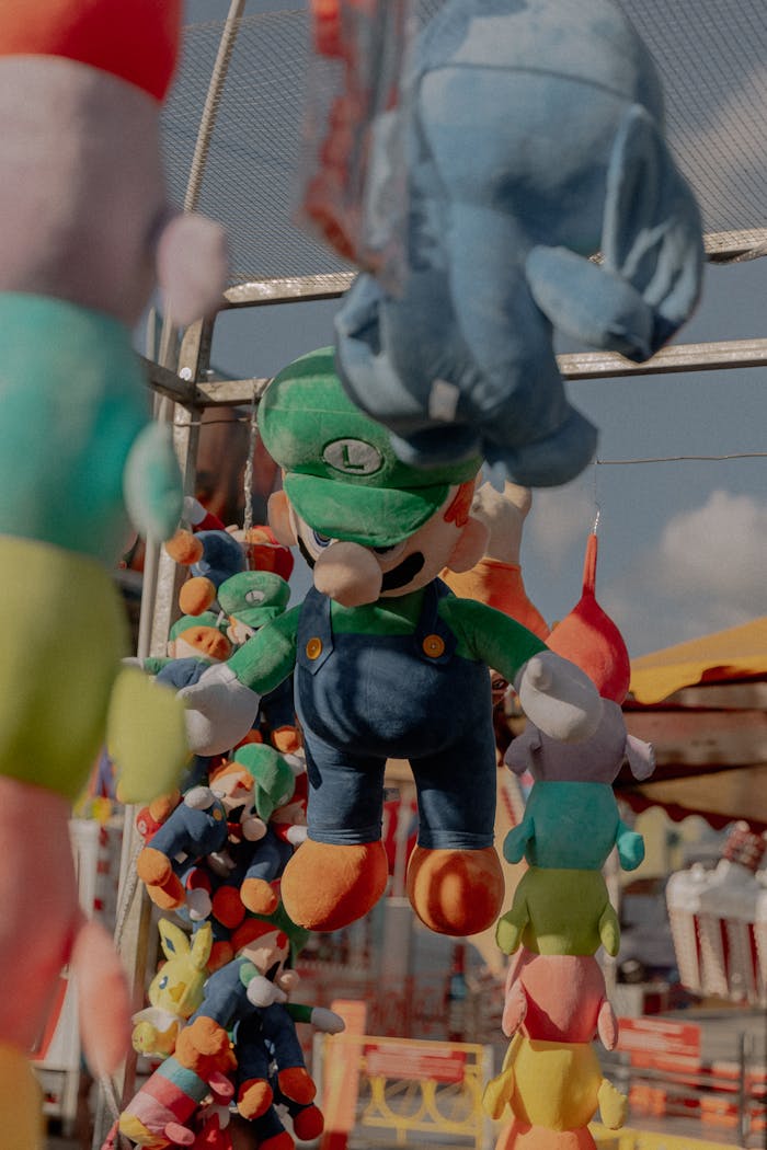 Hanging Luigi plush toys at a vibrant outdoor amusement park stall.